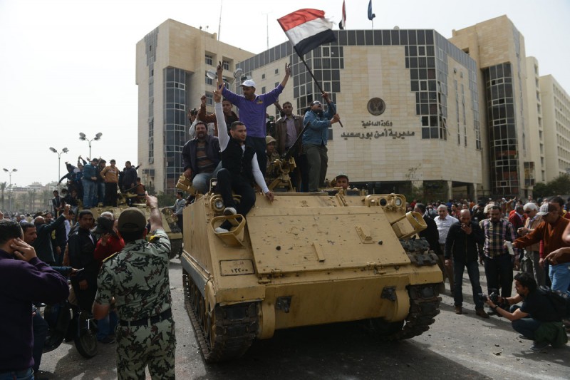 Egyptian protesters hold their national flag as they celebrate on an army tank outside Port Said’s security headquarters on March 8, 2013, following the withdrawal of police forces from their headquarters in the Suez Canal city that has been the target of protesters and transferred its protection to the military, the interior ministry said. © Image: Khaled Desouki/AFP/Getty Images, MPC Journal