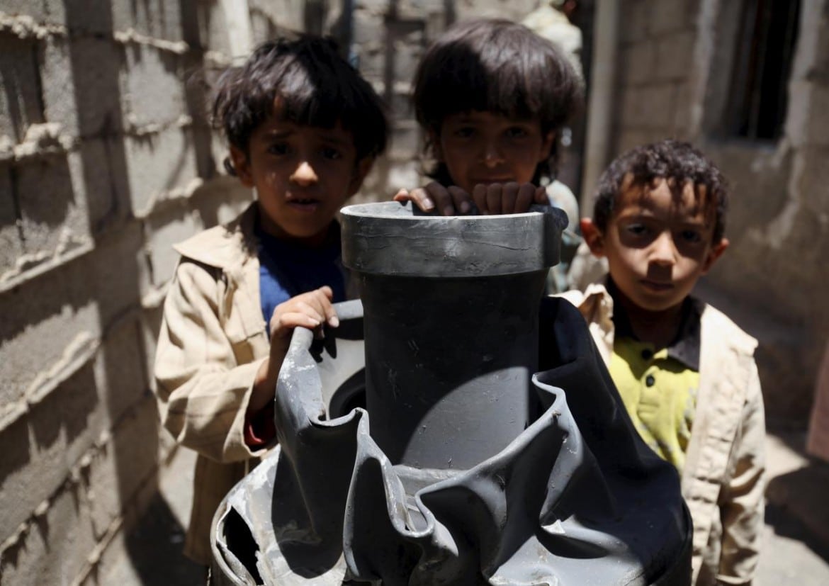 Children stand next to a shell which landed on their house from a nearby missile base after the base was struck by a Saudi-led coalition air strike, near Sanaa