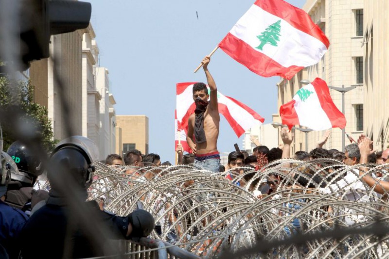Lebanese protesters wave the national flag in front of a barbed wire fence during a demonstration in the capital Beirut – © Image: AFP: Anwar Amro
